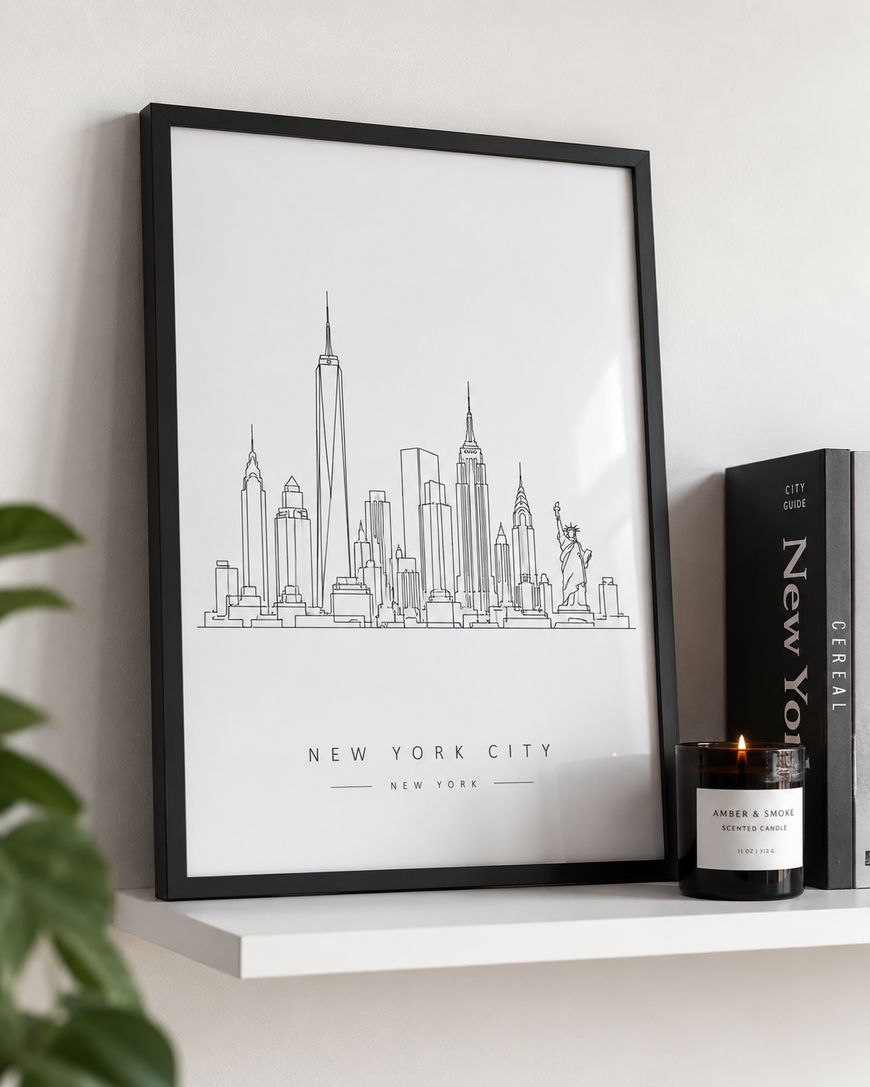 Framed minimalist line art of the New York City skyline on a white shelf, next to a black candle and books, including one labelled New York.
